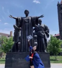 picture of woman in graduation gown in front of alma mater statue