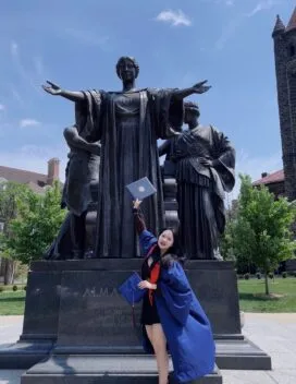 picture of woman in graduation gown in front of alma mater statue