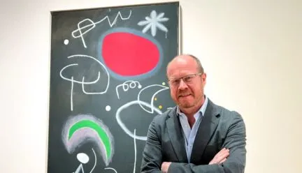 Man with glasses standing next to a painting done on a big canvas