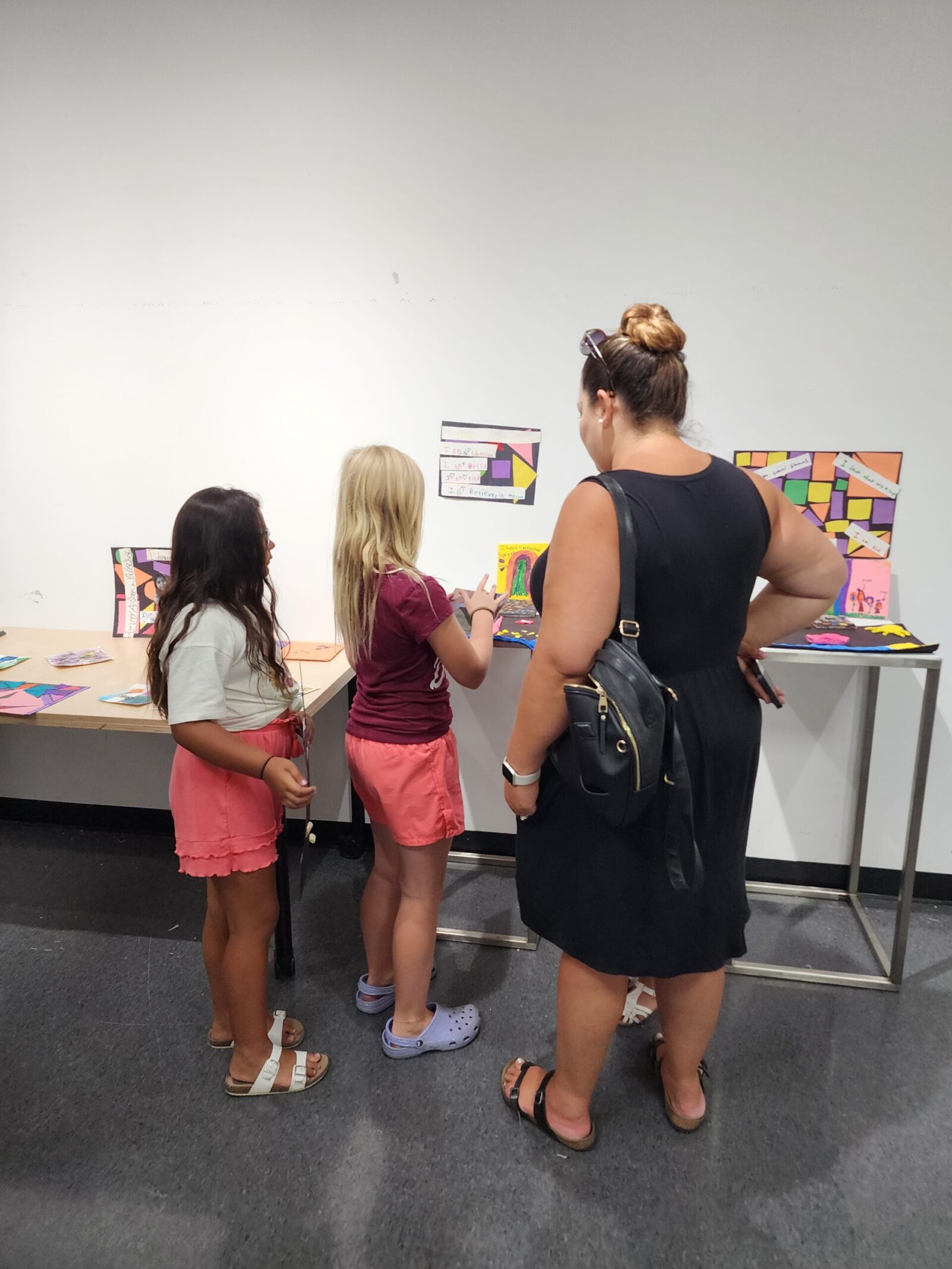An adult and two students looking at the student artwork on display.