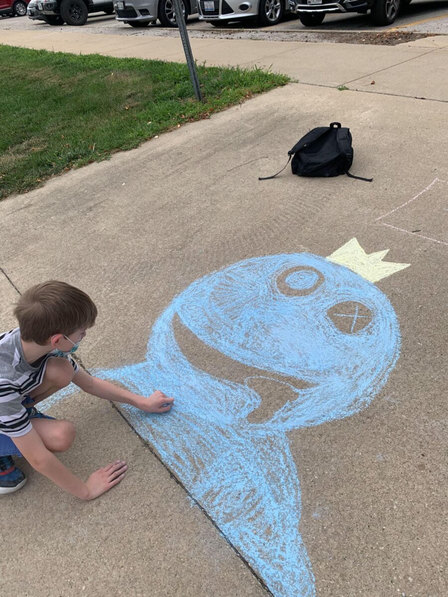 Student drawing a blue face on the sidewalk