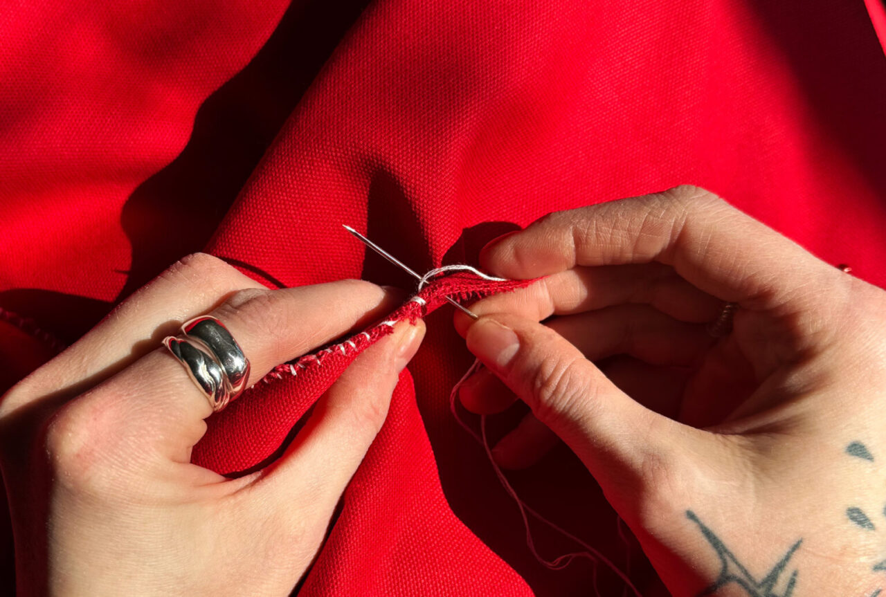 hands sewing red fabric