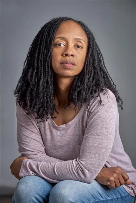 person seated with arms folded on legs, gray background