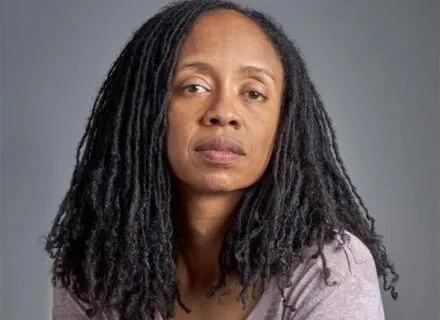 person seated with arms folded on legs, gray background