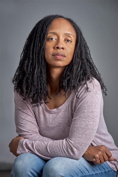 person seated with arms folded on legs, gray background