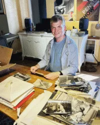 person works at table with lots of old photographs and manuscripts