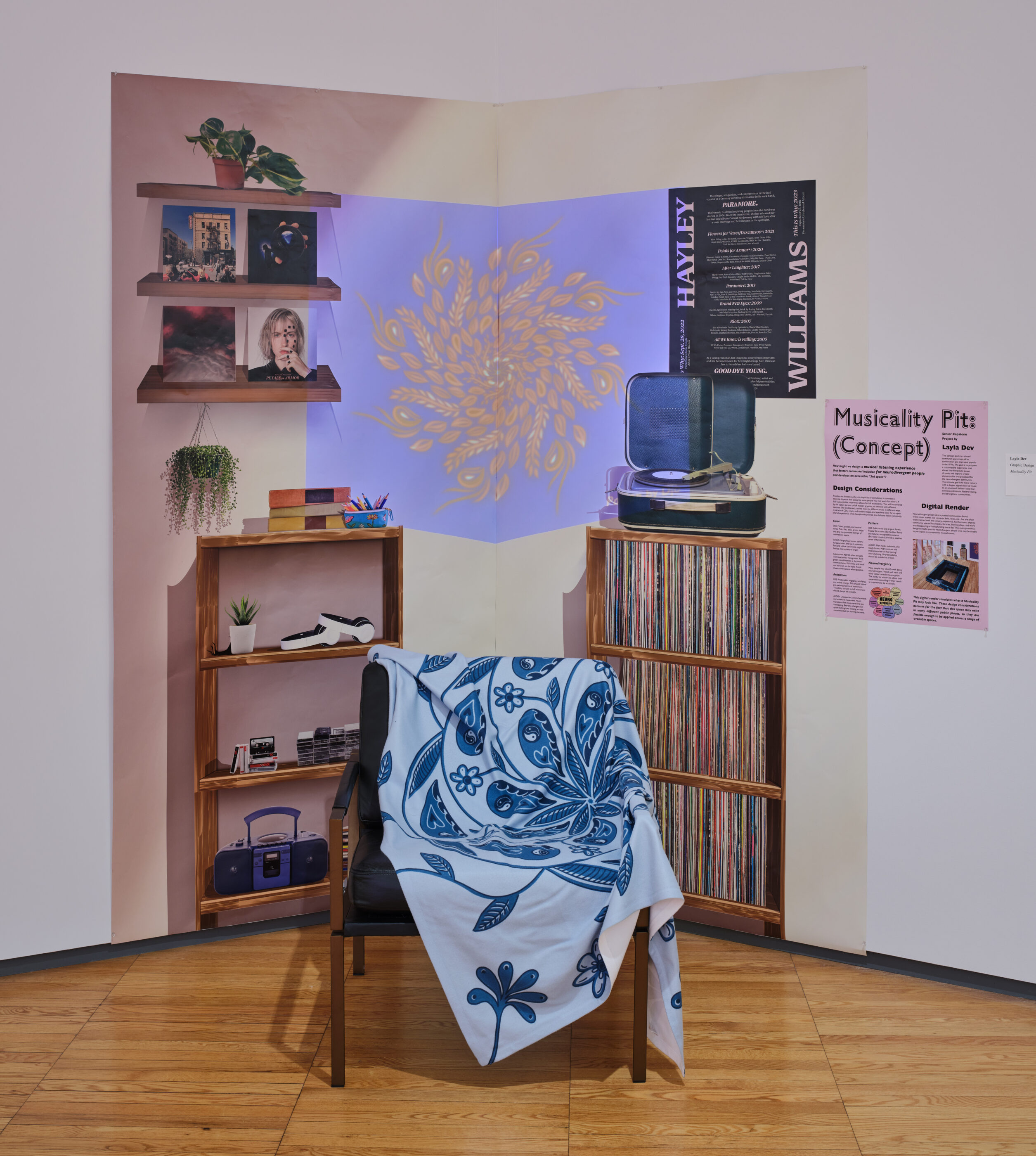 mixed media artwork displayed in gallery with chair, shelves and various books and other items” slot=