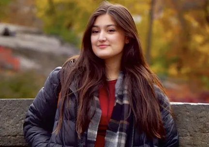 image of a student by a fence outside in the fall