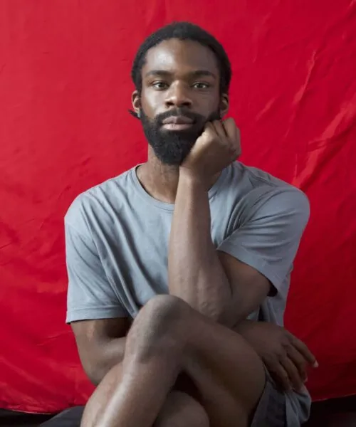 Dare sits with his legs crossed in front of a red draped background