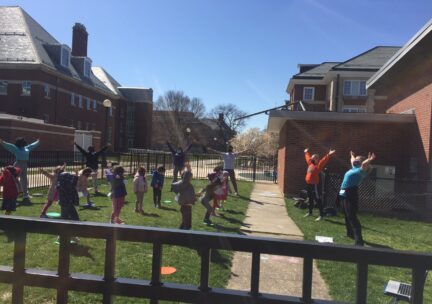 Children extend their arms out as they dance outdoors