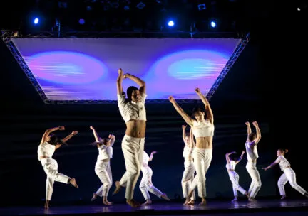 Dancers in white with arms up under purple square