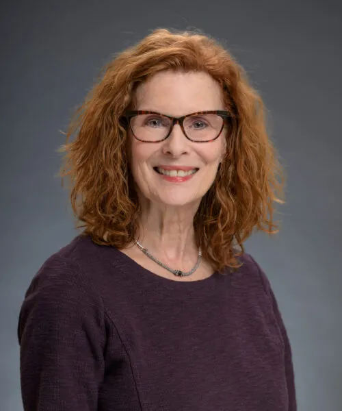A headshot of Rebecca, wearing a bright orange scarf