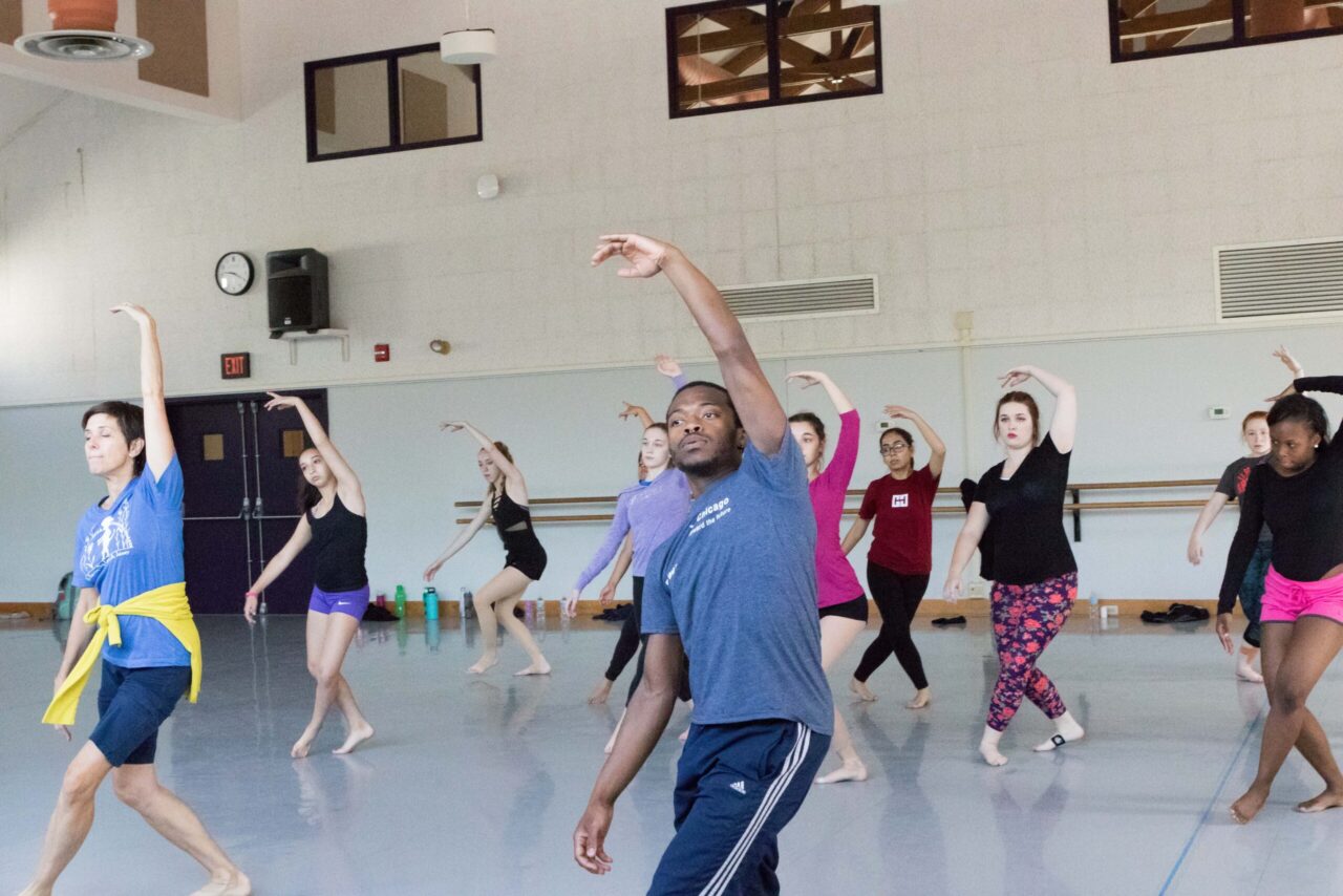A group of young dancers reach their left arm up above their heads