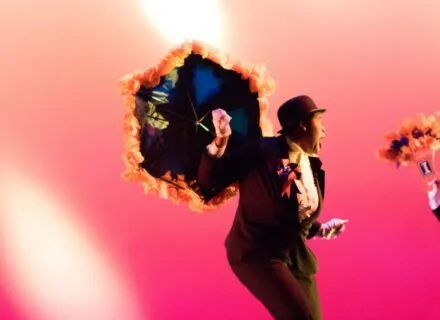 Dancer holding decorated umbrella against pink background