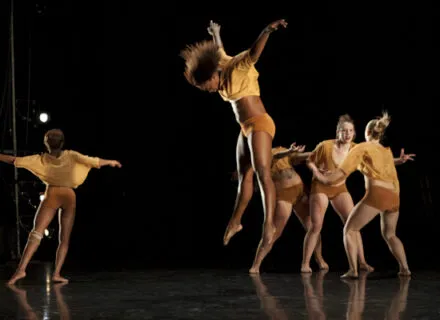 One Dancer in midair with arms up and other dancers on the floor
