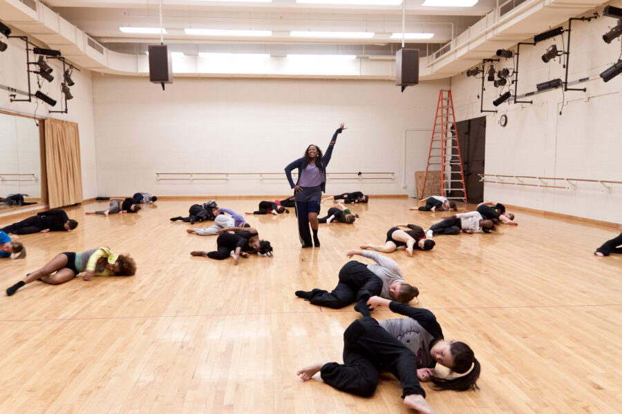 T. Lang standing in the center of the studio with students laying in a pose on the floor