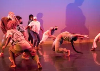 A dancers reaches back in a back bend as other dancers surround her