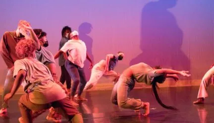 A dancers reaches back in a back bend as other dancers surround her