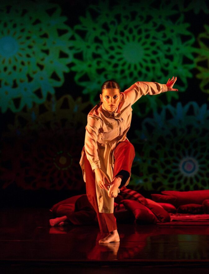 A lone dancer reaches their right arm forward in front of a green scrim