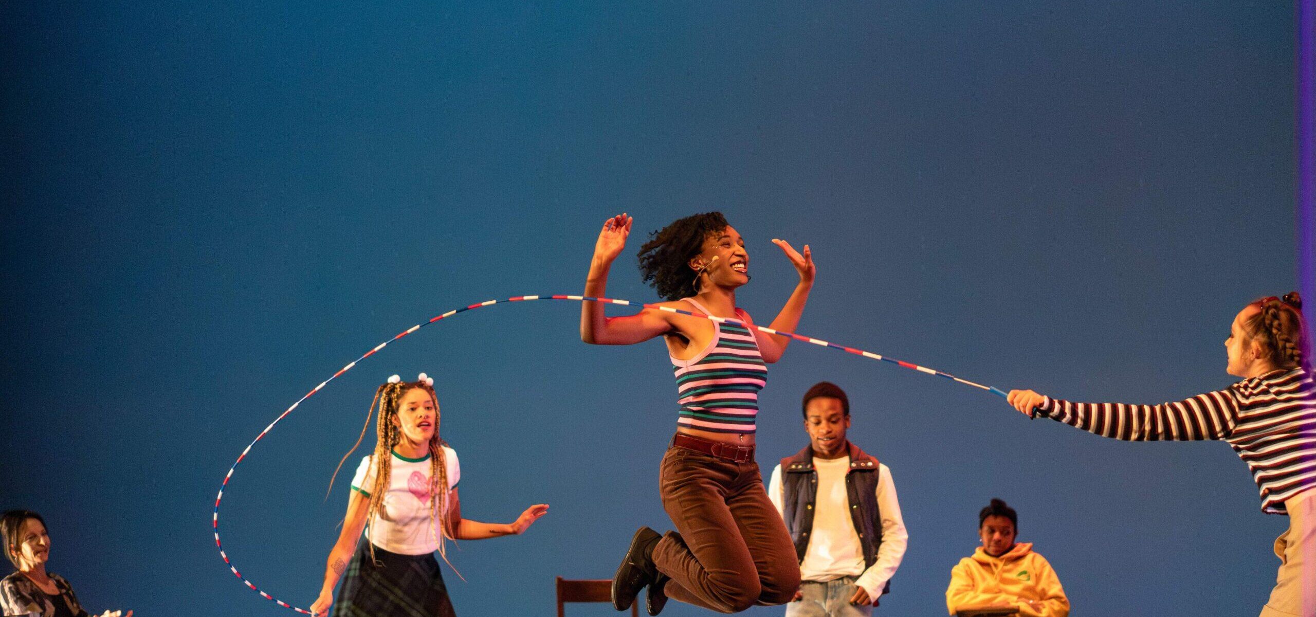 Dancers on stage with one dancer in a jump with a jumprope
