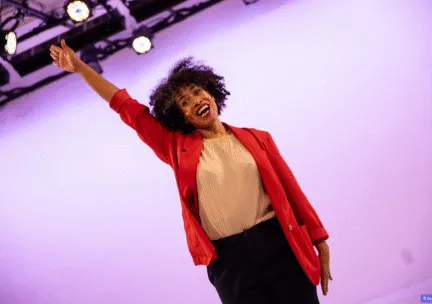 Leslie reaches her right hand up in a red blazer