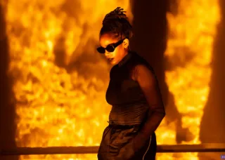 angie pittman wearing all black and sunglasses with a fire-orange projection background