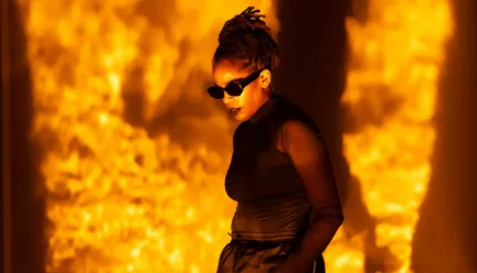 angie pittman wearing all black and sunglasses with a fire-orange projection background