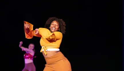 a dancer dressed in orange throws her arms up and sways