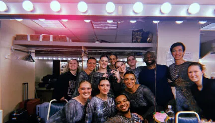 many people gathered in a dresssing room smiling into a mirror