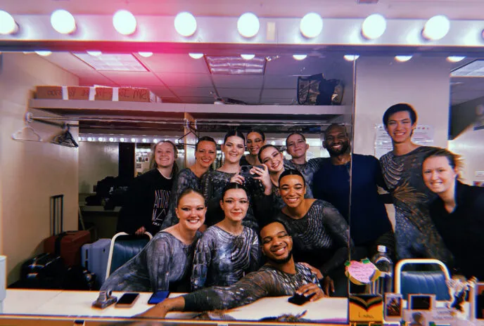 many people gathered in a dresssing room smiling into a mirror