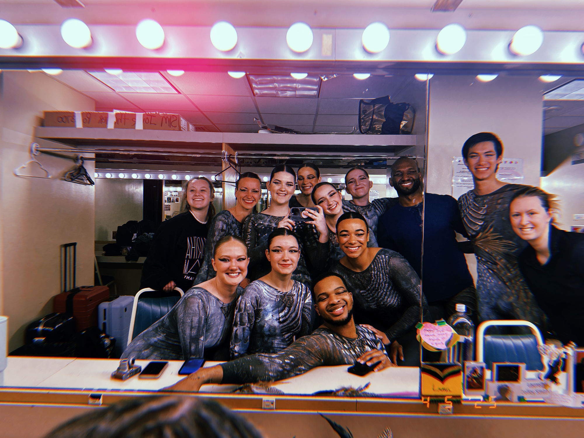 many people gathered in a dresssing room smiling into a mirror