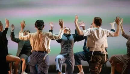 dancers crouch in a huddle with their arms up
