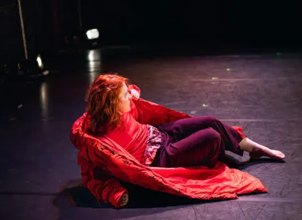 A dancer lies on the floor with a red coat