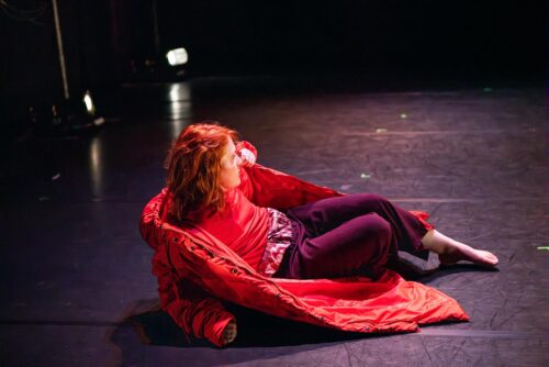 A dancer lies on the floor with a red coat