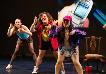 A dancer jumps in the background as another dancer balances on one leg in the foreground