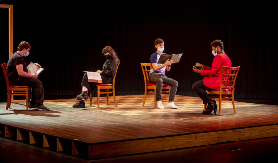 Four actors reading scripts from chairs