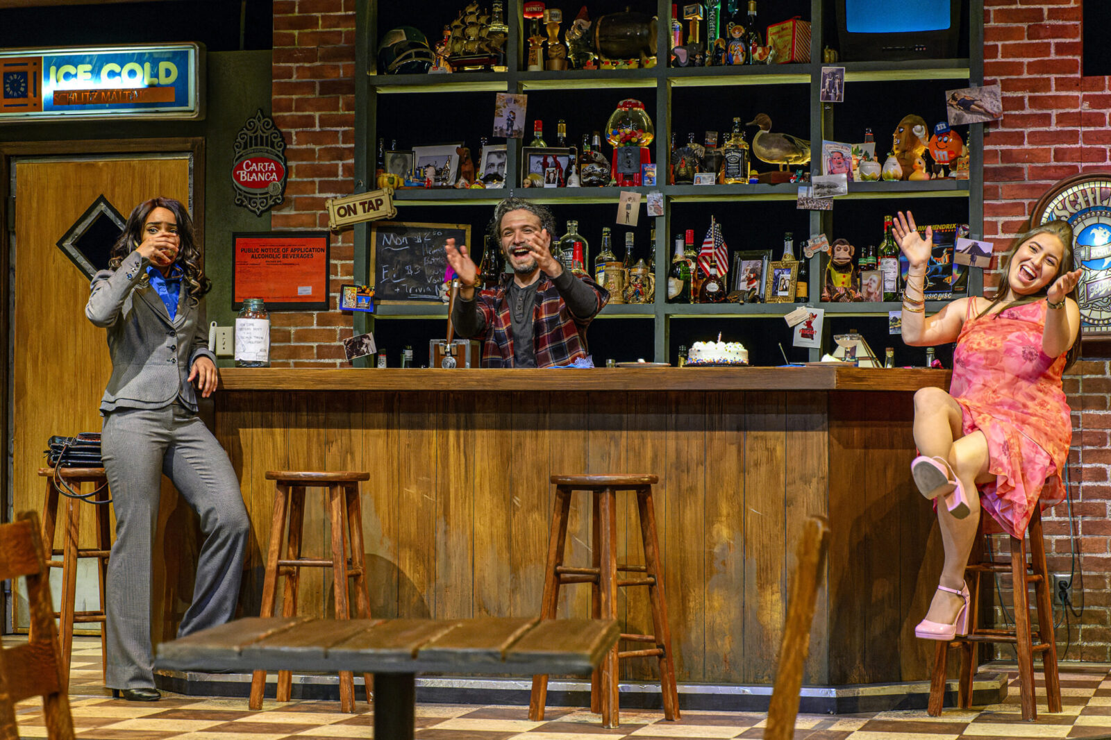 3 actors on stage at a large bar, looking like they are celebrating something