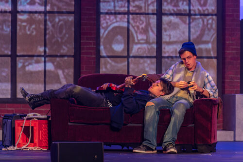 2 actors on stage laying on a couche