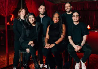 6 people sitting and standing in a theatre wearing black