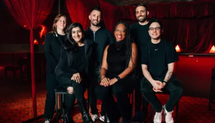 6 people sitting and standing in a theatre wearing black