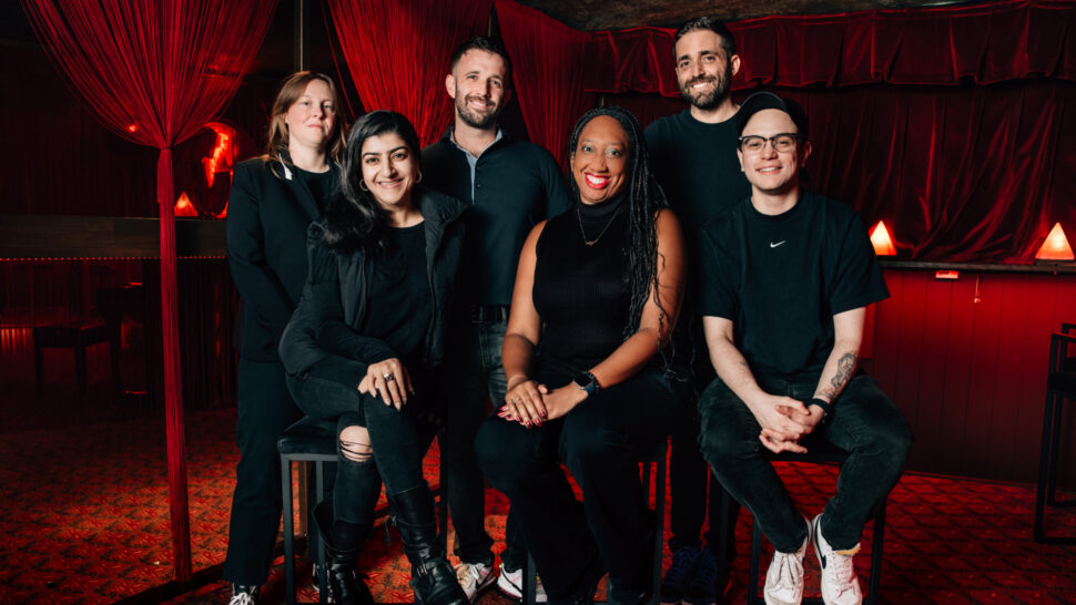 6 people sitting and standing in a theatre wearing black