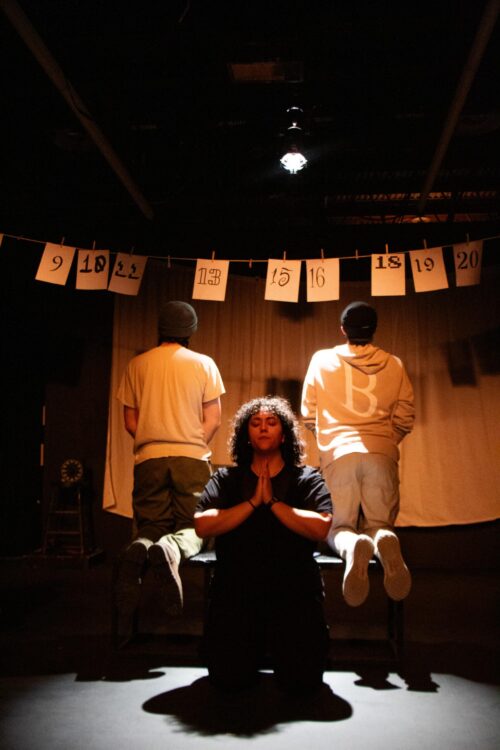person kneeling onstage with two people behind facing back
