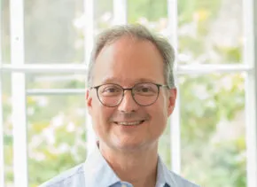 Man in blue shirt and glasses smiling in front of window