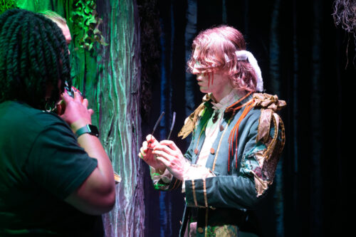 a person in prince-like costume shows audience members an item