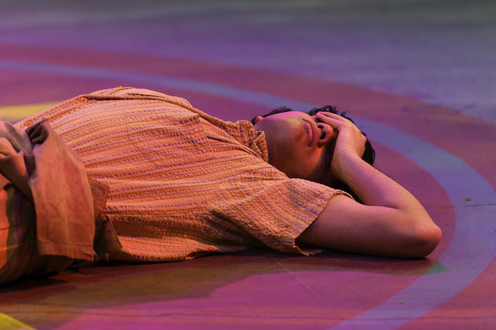 a person lies on the stage covering their eyes