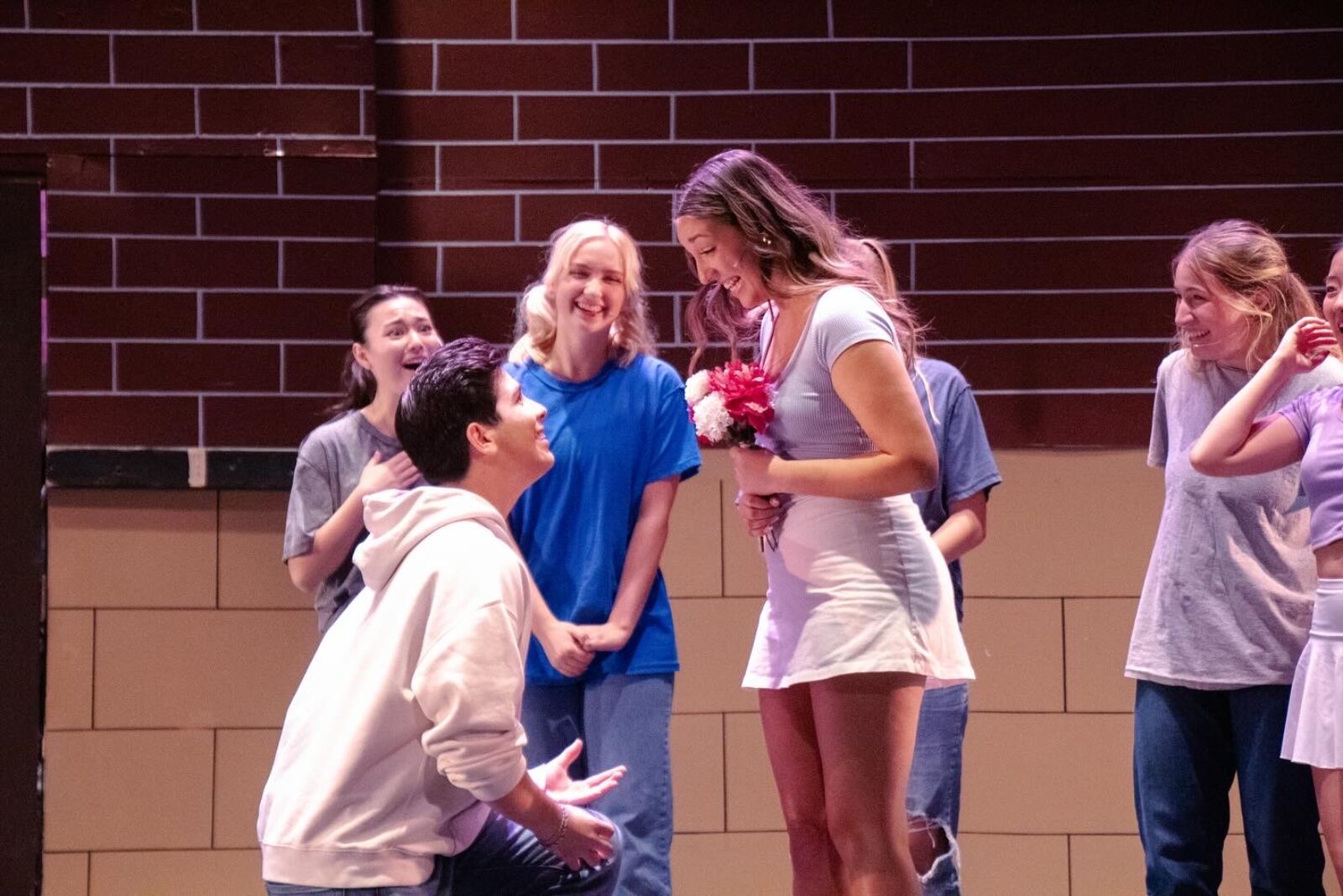several people onstage, one on knees in front of a person with flowers