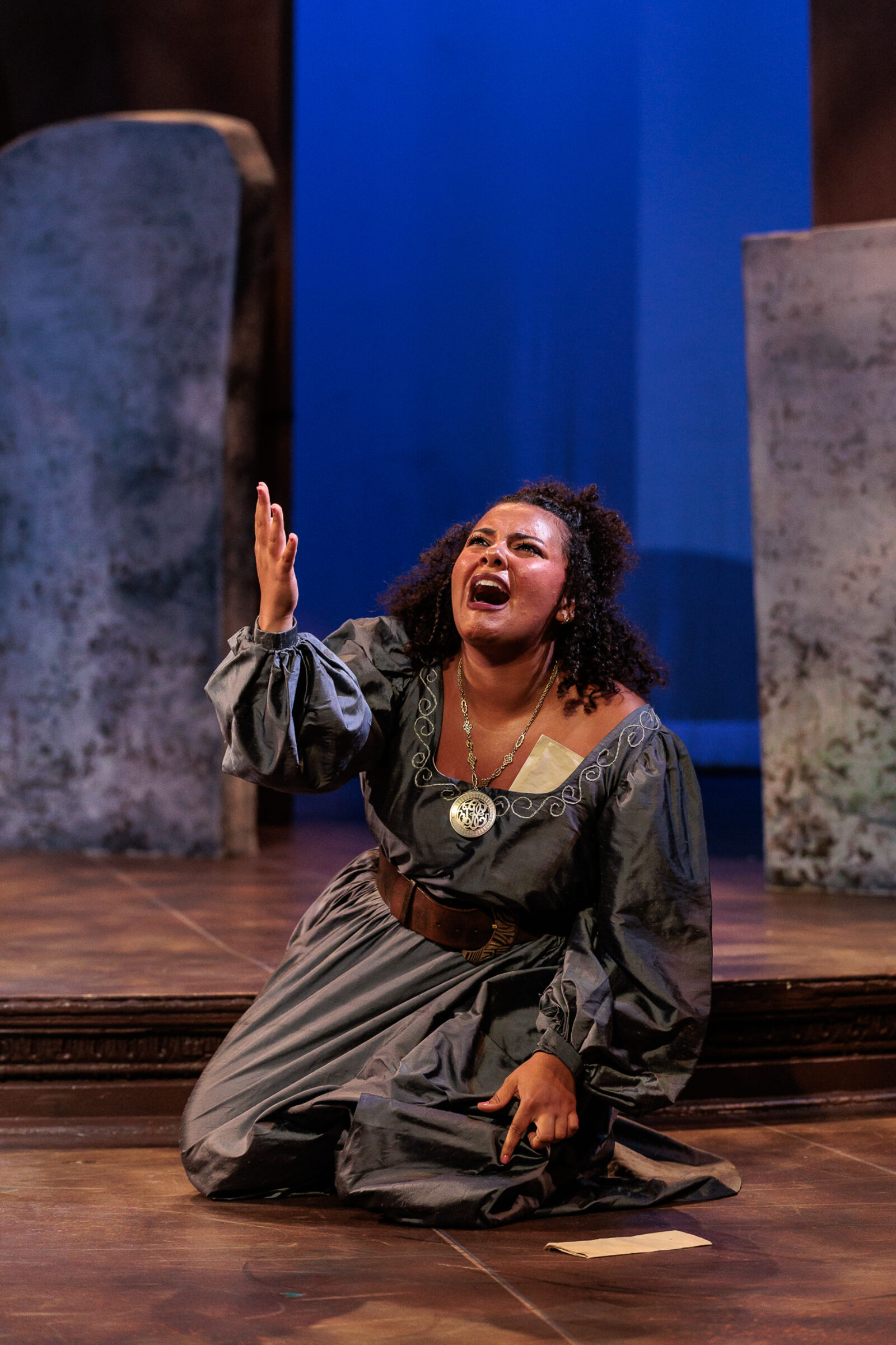 a person onstage on their knees with arm outstretched, speaking