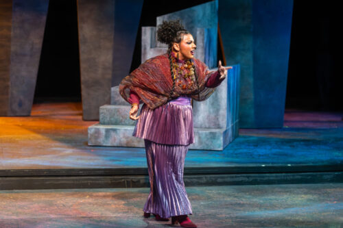 a person in costume walking across a stage speaking and pointing to something