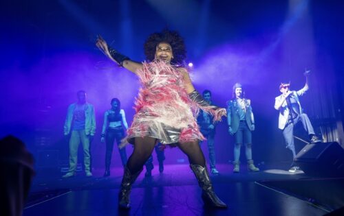 a person onstage playing air guitar and backlit with rock lighting