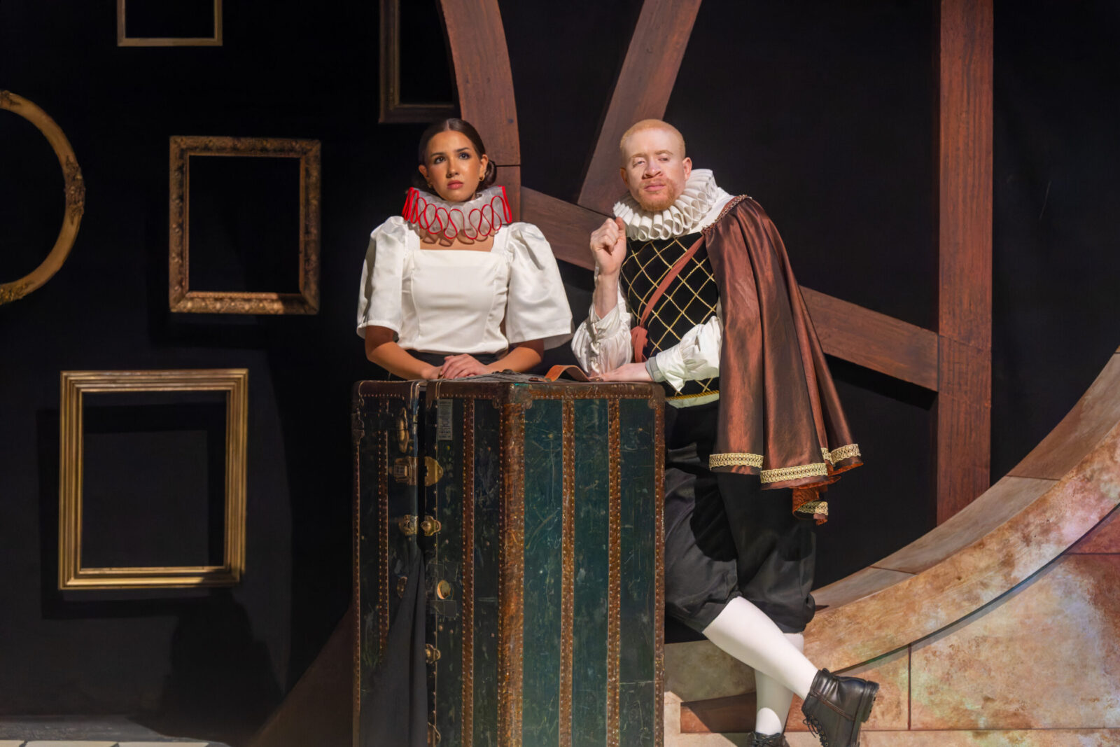 person sits on stage and speaks with arms outstretched 